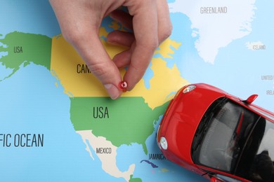 Photo of Road trip concept. Woman attaching pin to world map near car model, top view