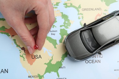 Photo of Road trip concept. Woman attaching pin to world map near car model, top view