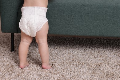 Photo of Cute little baby standing near sofa at home, closeup. Space for text