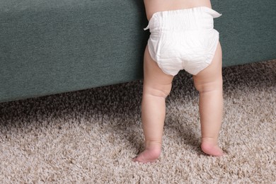 Photo of Cute little baby standing near sofa at home, closeup. Space for text
