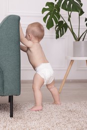 Photo of Cute little baby standing near sofa at home