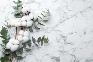Photo of Eucalyptus branches and cotton flowers on white marble table, flat lay. Space for text