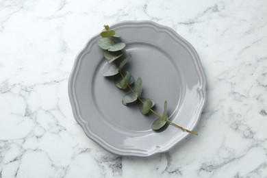 Photo of Stylish plate and eucalyptus branch on white marble table, top view