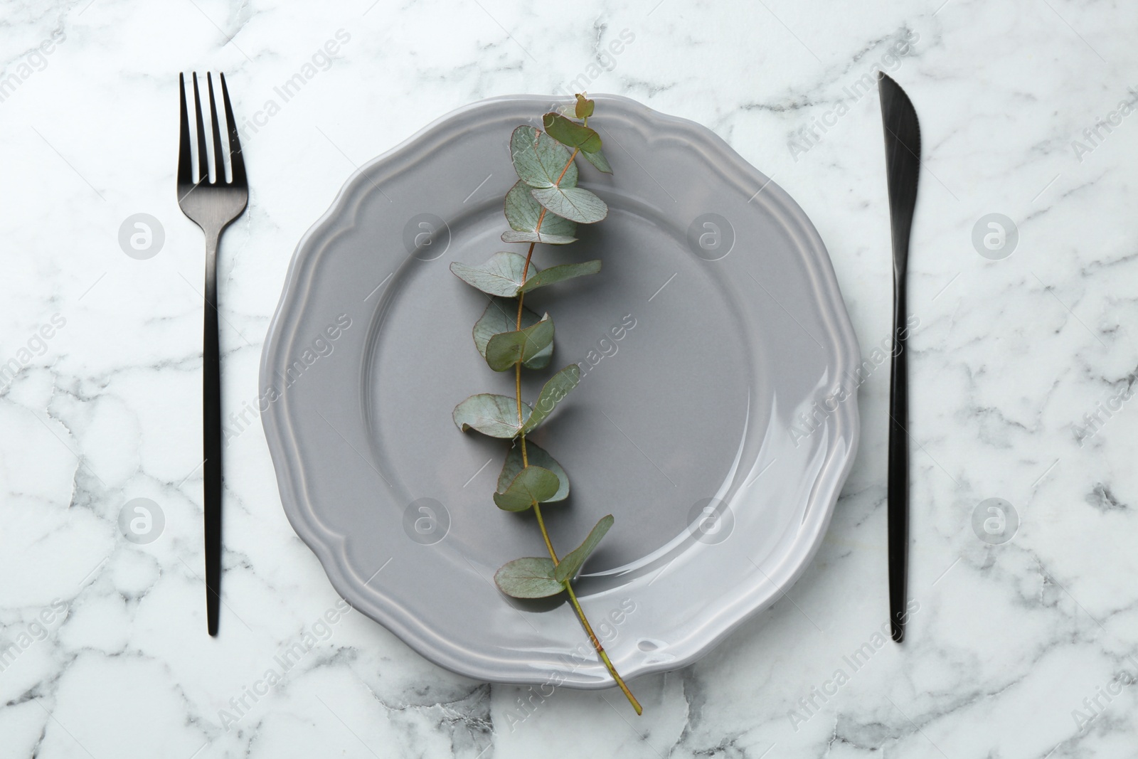 Stylish plate, cutlery and eucalyptus branch on white marble table, flat lay Photo of Stylish plate, cutlery and eucalyptus branch on white marble table, flat lay