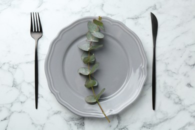 Photo of Stylish plate, cutlery and eucalyptus branch on white marble table, flat lay