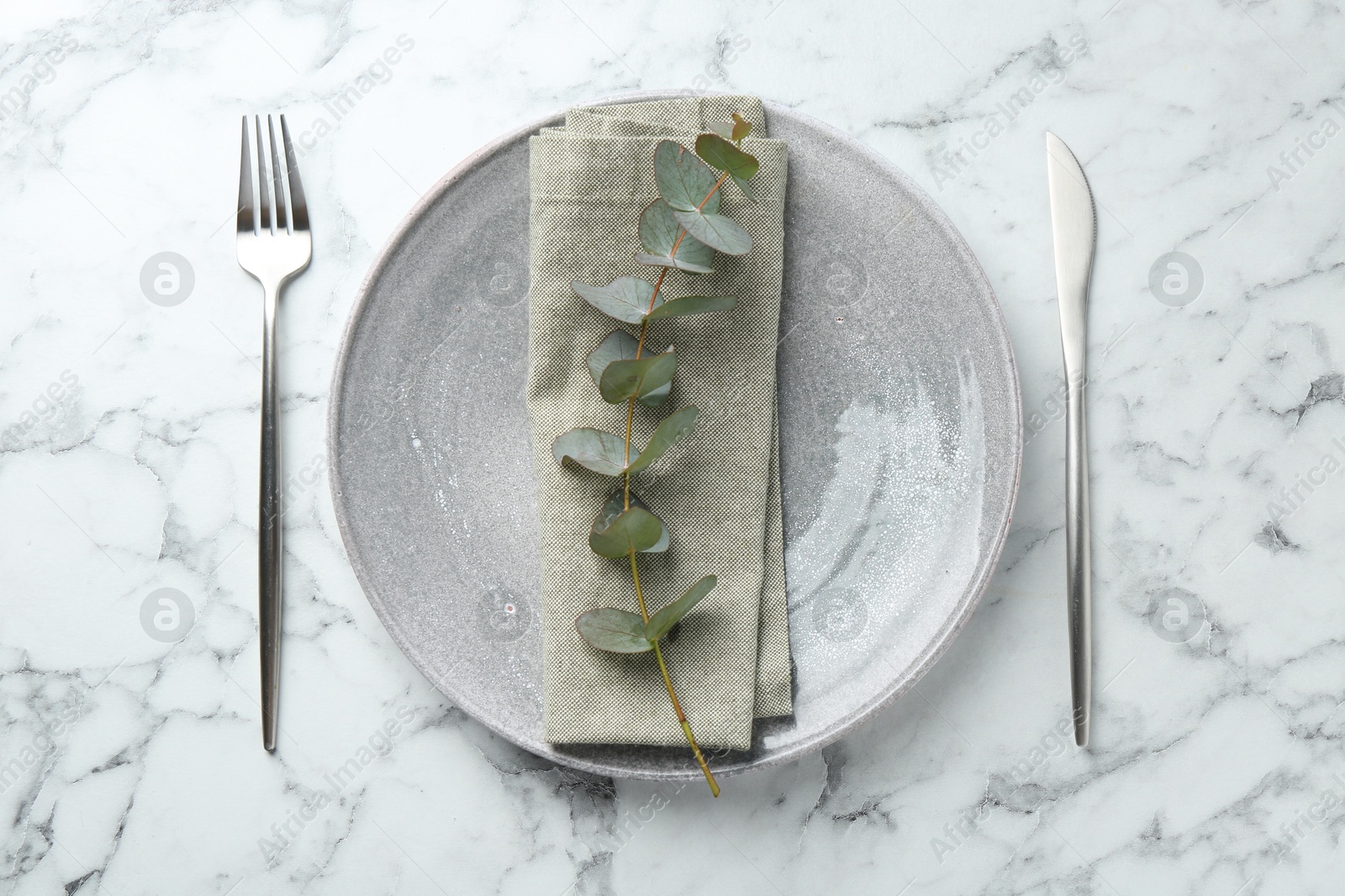 Stylish plate, napkin, cutlery and eucalyptus branch on white marble table, flat lay Photo of Stylish plate, napkin, cutlery and eucalyptus branch on white marble table, flat lay