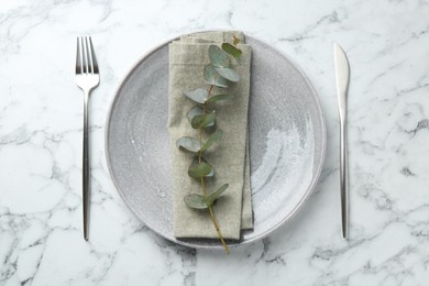 Photo of Stylish plate, napkin, cutlery and eucalyptus branch on white marble table, flat lay