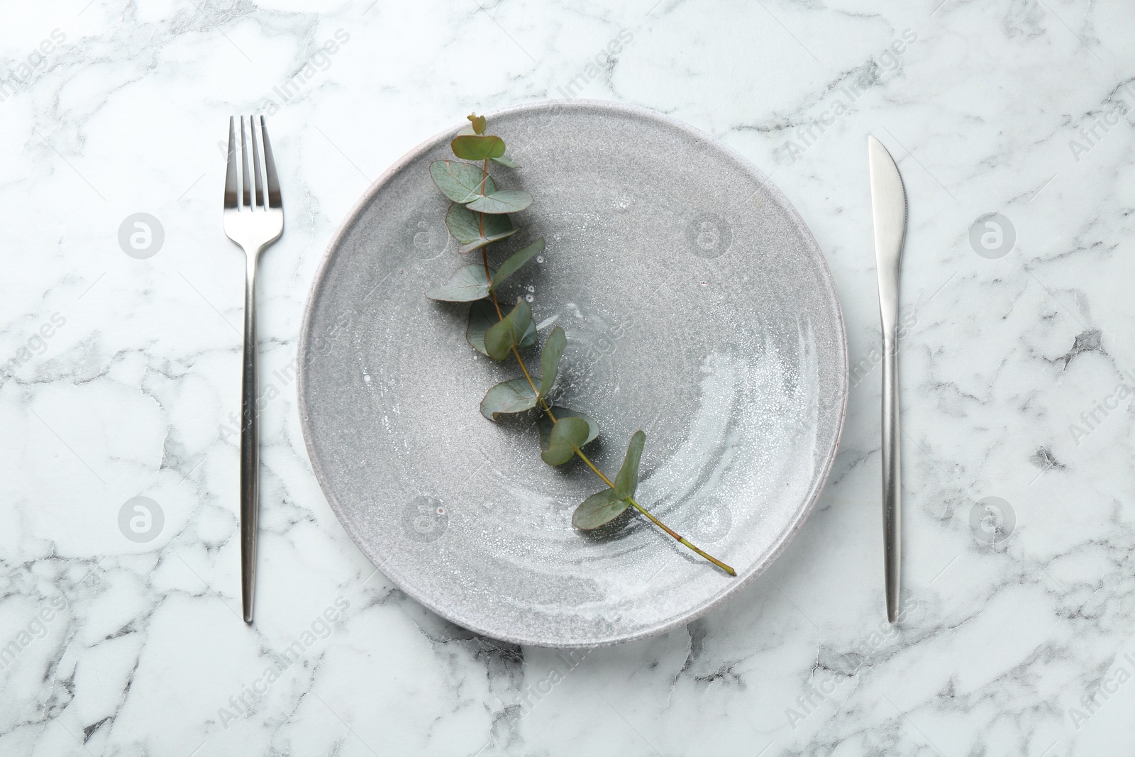 Stylish plate, cutlery and eucalyptus branch on white marble table, flat lay Photo of Stylish plate, cutlery and eucalyptus branch on white marble table, flat lay