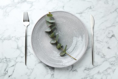 Photo of Stylish plate, cutlery and eucalyptus branch on white marble table, flat lay