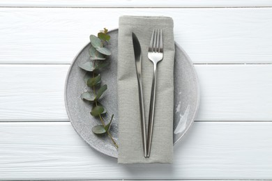 Photo of Stylish plate, napkin, cutlery and eucalyptus branch on white wooden table, top view
