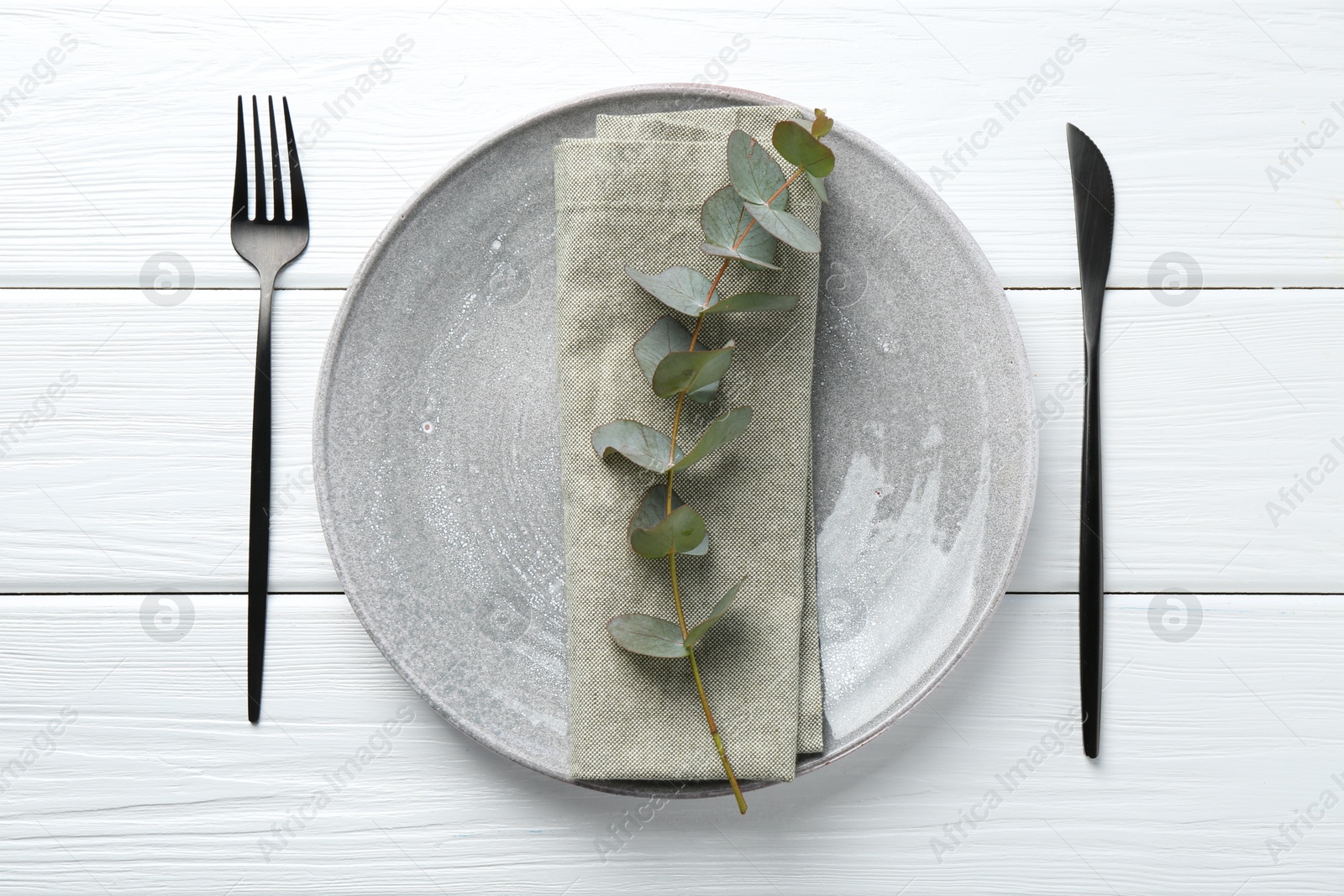 Stylish plate, napkin, cutlery and eucalyptus branch on white wooden table, flat lay Photo of Stylish plate, napkin, cutlery and eucalyptus branch on white wooden table, flat lay