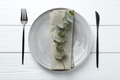 Photo of Stylish plate, napkin, cutlery and eucalyptus branch on white wooden table, flat lay