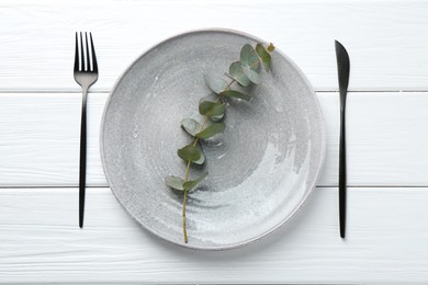 Photo of Stylish plate, cutlery and eucalyptus branch on white wooden table, flat lay