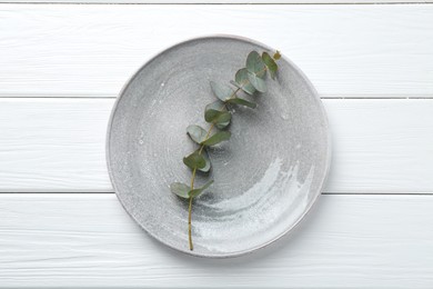 Photo of Stylish plate and eucalyptus branch on white wooden table, top view