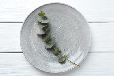 Photo of Stylish plate and eucalyptus branch on white wooden table, top view