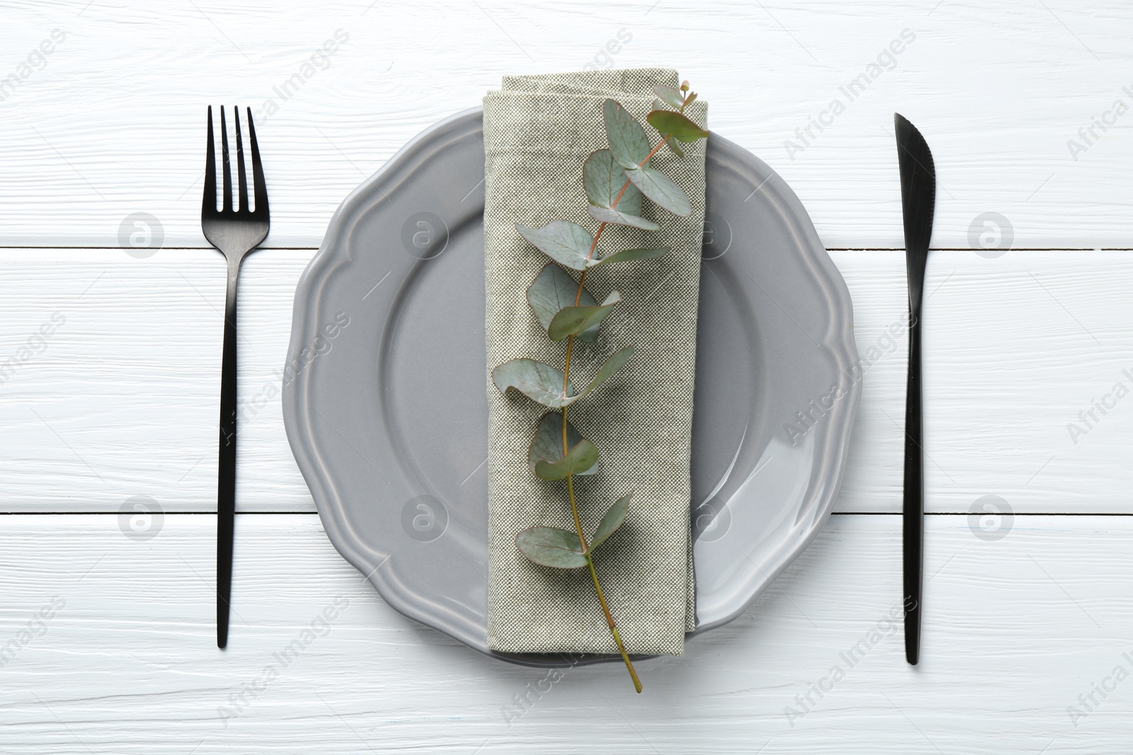 Stylish plate, napkin, cutlery and eucalyptus branch on white wooden table, flat lay Photo of Stylish plate, napkin, cutlery and eucalyptus branch on white wooden table, flat lay