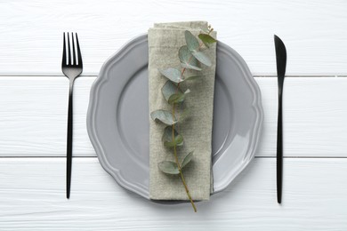 Photo of Stylish plate, napkin, cutlery and eucalyptus branch on white wooden table, flat lay