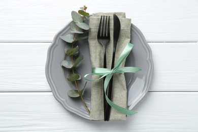 Photo of Stylish plate, napkin, cutlery and eucalyptus branch on white wooden table, top view