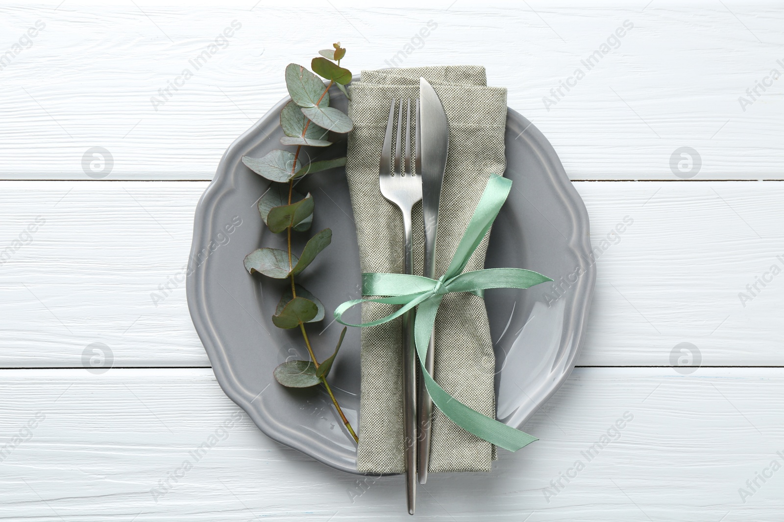 Photo of Stylish plate, napkin, cutlery and eucalyptus branch on white wooden table, top view