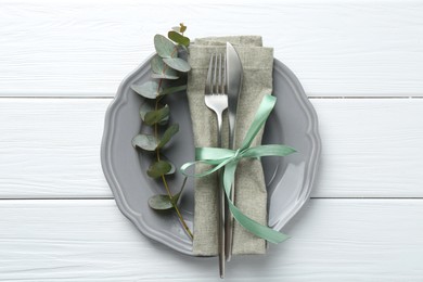 Photo of Stylish plate, napkin, cutlery and eucalyptus branch on white wooden table, top view