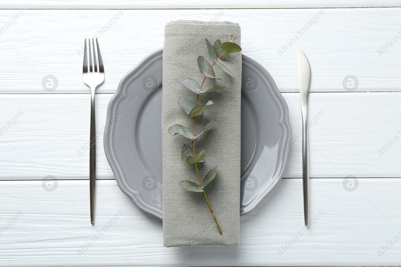 Stylish plate, napkin, cutlery and eucalyptus branch on white wooden table, flat lay Photo of Stylish plate, napkin, cutlery and eucalyptus branch on white wooden table, flat lay