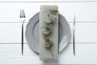 Photo of Stylish plate, napkin, cutlery and eucalyptus branch on white wooden table, flat lay
