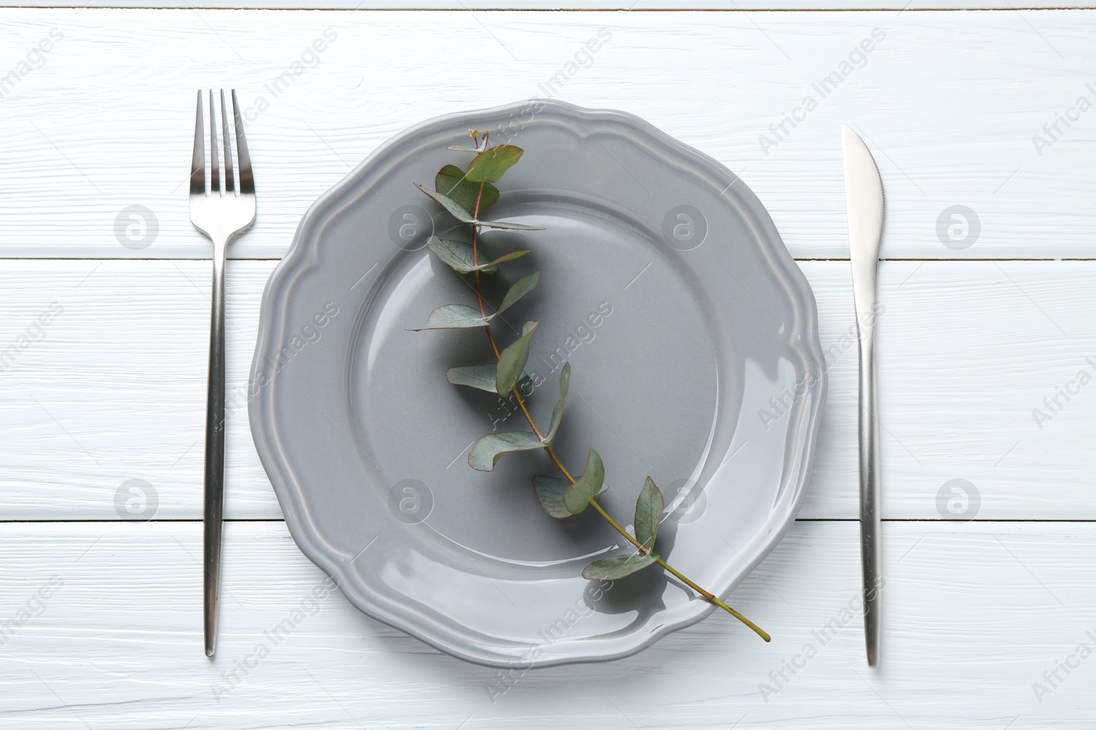 Stylish plate, cutlery and eucalyptus branch on white wooden table, flat lay Photo of Stylish plate, cutlery and eucalyptus branch on white wooden table, flat lay