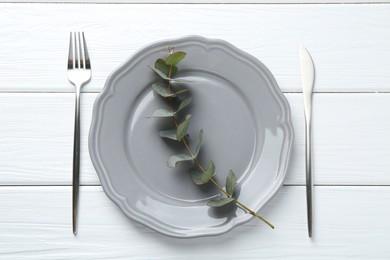 Photo of Stylish plate, cutlery and eucalyptus branch on white wooden table, flat lay