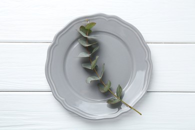 Photo of Stylish plate and eucalyptus branch on white wooden table, top view