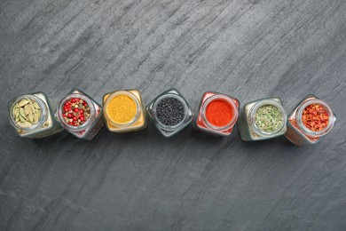 Photo of Different aromatic spices in jars on black table, flat lay