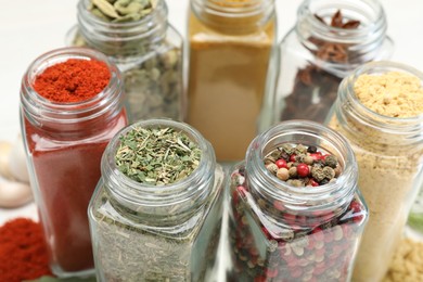 Photo of Different aromatic spices in jars on white table, closeup