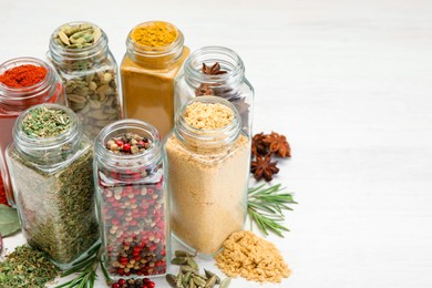 Photo of Different aromatic spices in jars on white table, closeup