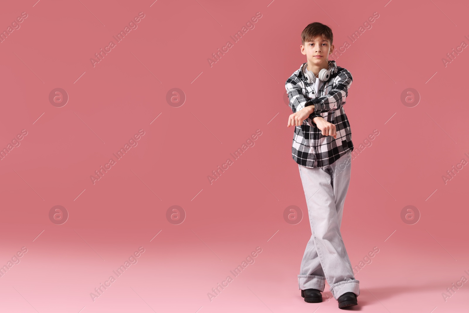 Photo of Boy with headphones in stylish clothes dancing on pink background, space for text