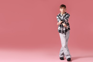 Photo of Boy with headphones in stylish clothes dancing on pink background, space for text