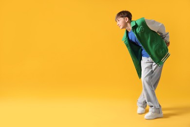 Photo of Boy in stylish clothes dancing on orange background, space for text