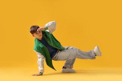 Photo of Boy in stylish clothes dancing on orange background