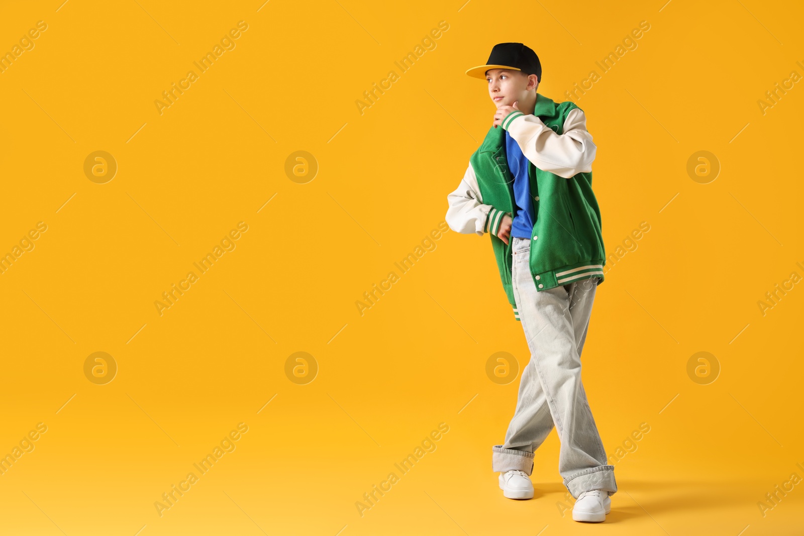 Boy in stylish clothes dancing on orange background, space for text Photo of Boy in stylish clothes dancing on orange background, space for text