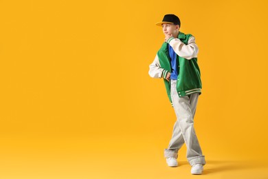 Photo of Boy in stylish clothes dancing on orange background, space for text