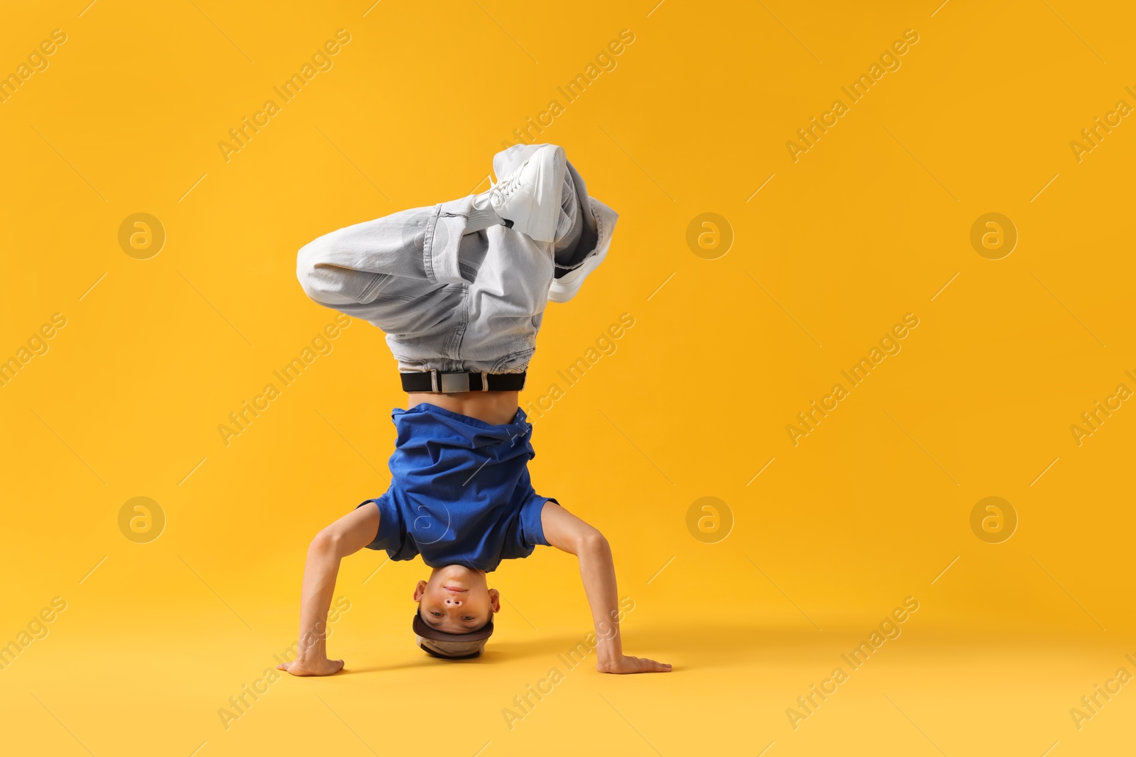 Photo of Boy in stylish clothes dancing on orange background, space for text