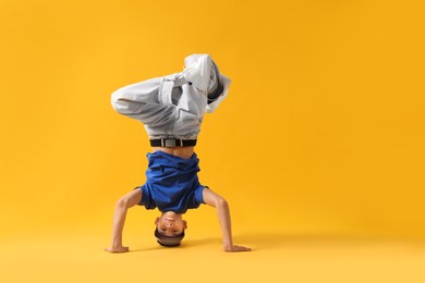 Photo of Boy in stylish clothes dancing on orange background, space for text