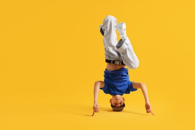 Photo of Boy in stylish clothes dancing on orange background, space for text