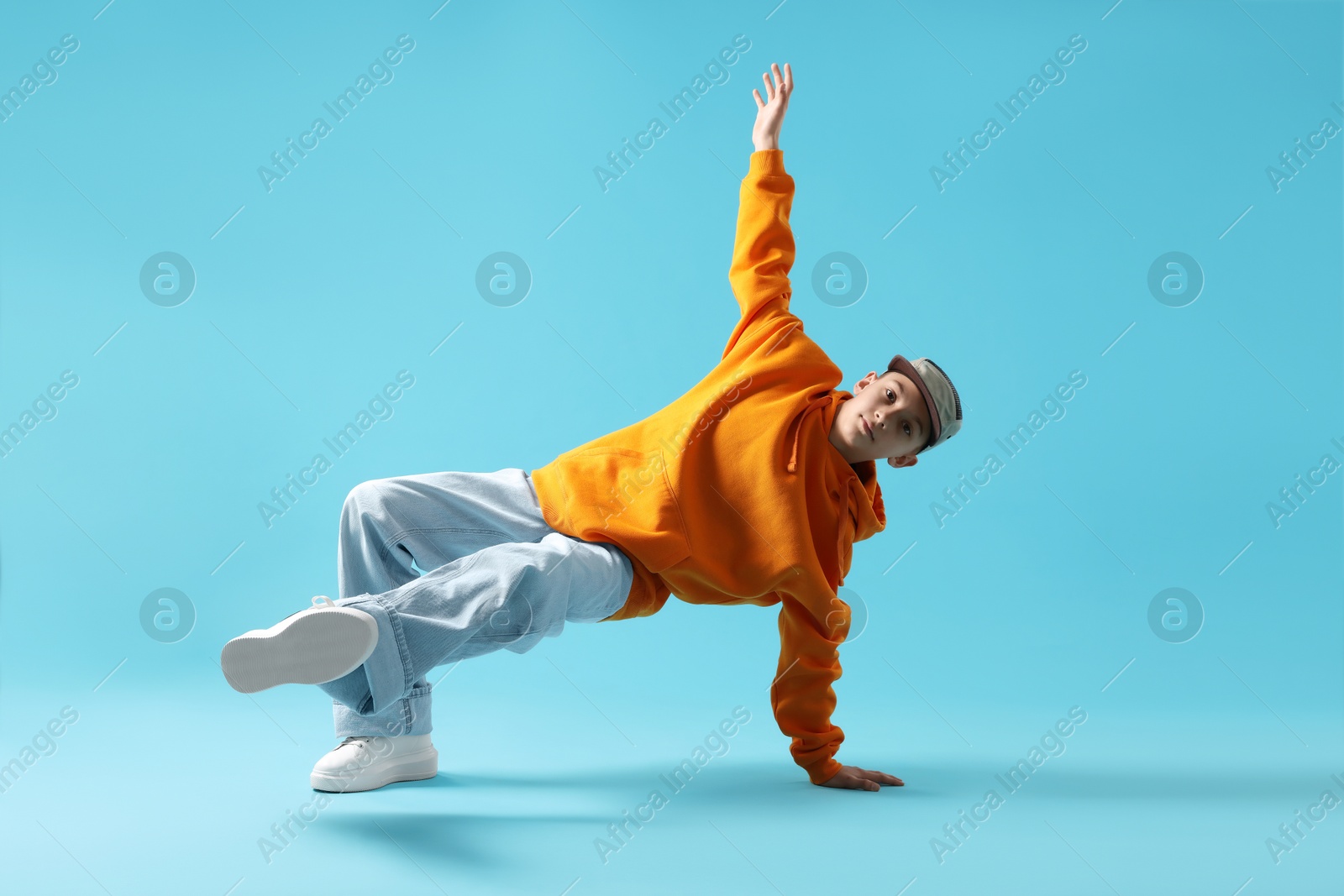 Boy in stylish clothes dancing on light blue background Photo of Boy in stylish clothes dancing on light blue background