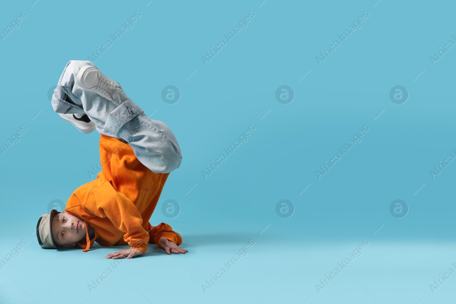 Photo of Boy in stylish clothes dancing on light blue background, space for text