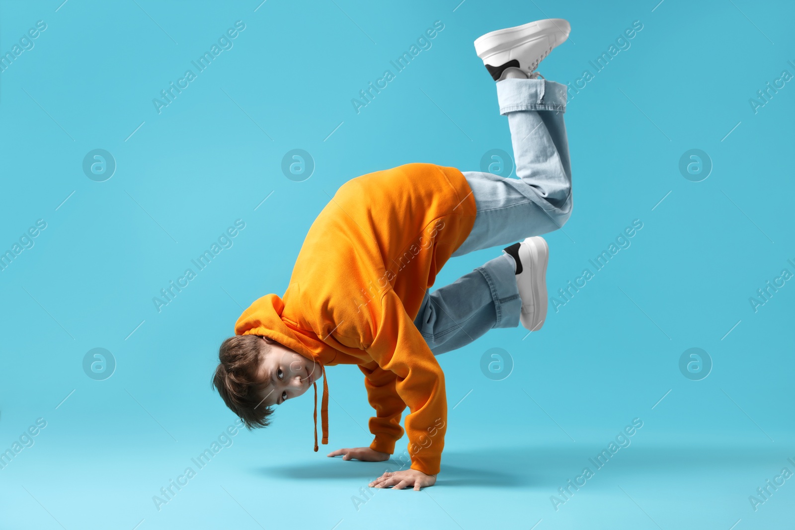 Boy in stylish clothes dancing on light blue background Photo of Boy in stylish clothes dancing on light blue background