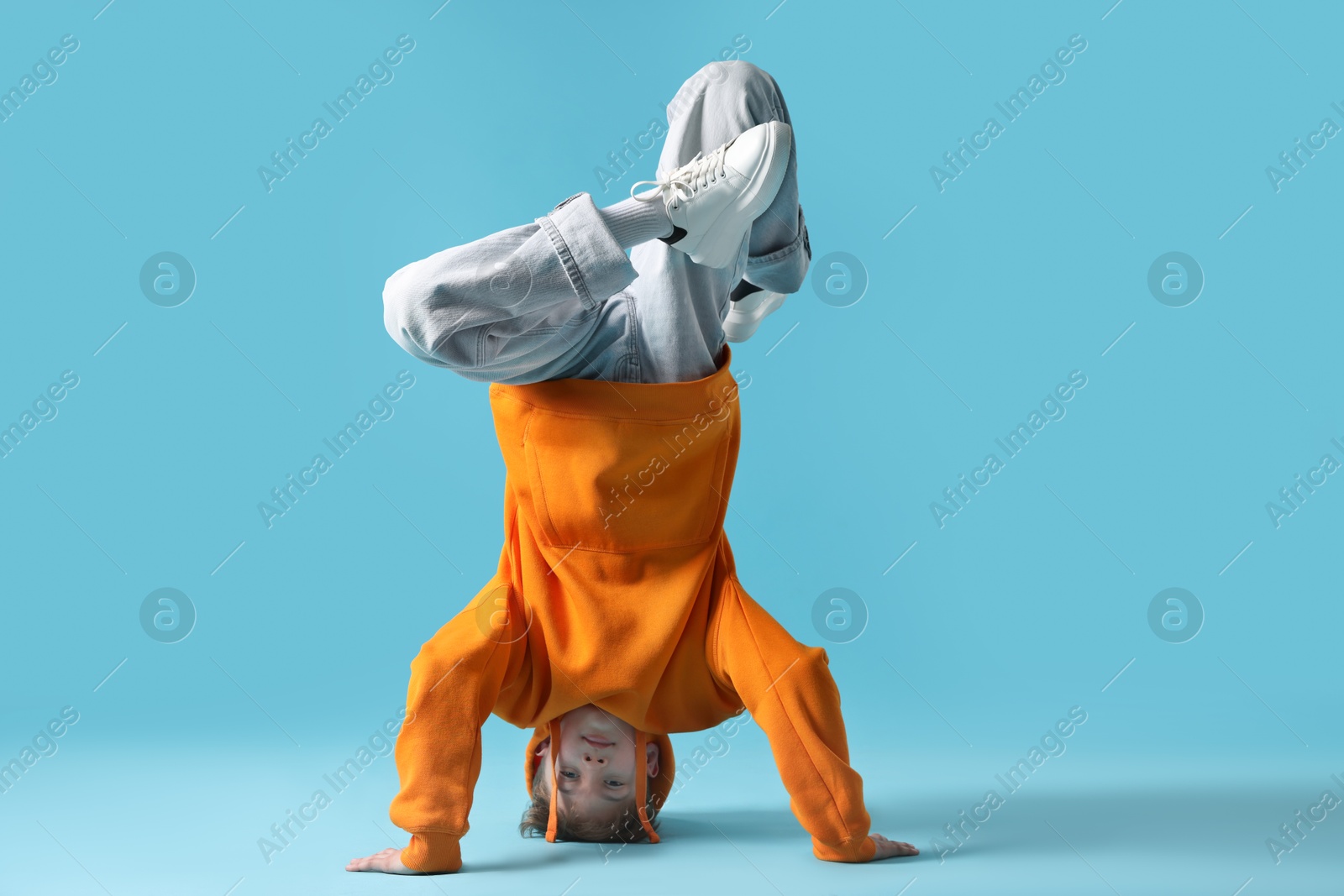 Boy in stylish clothes dancing on light blue background Photo of Boy in stylish clothes dancing on light blue background