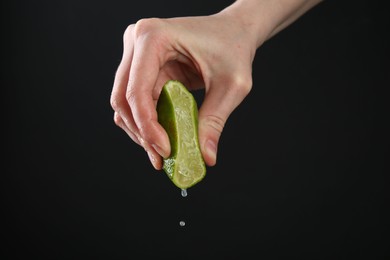Photo of Woman squeezing lime on black background, closeup