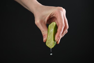 Photo of Woman squeezing lime on black background, closeup
