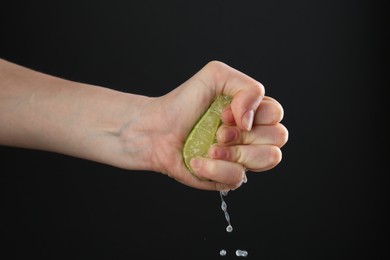Photo of Woman squeezing lime on black background, closeup