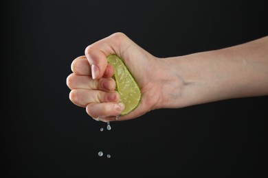 Photo of Woman squeezing lime on black background, closeup