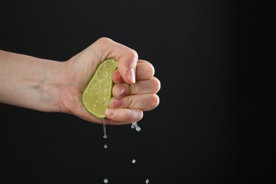 Photo of Woman squeezing lime on black background, closeup. Space for text